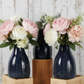 Set of three dark blue textured vases with plants on a white brick wall background