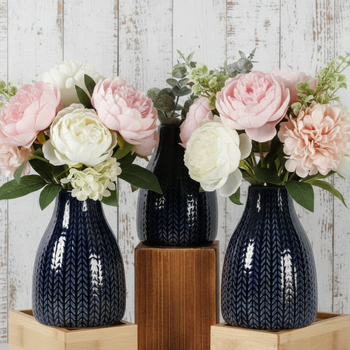 Set of three dark blue textured vases with plants on a white brick wall background