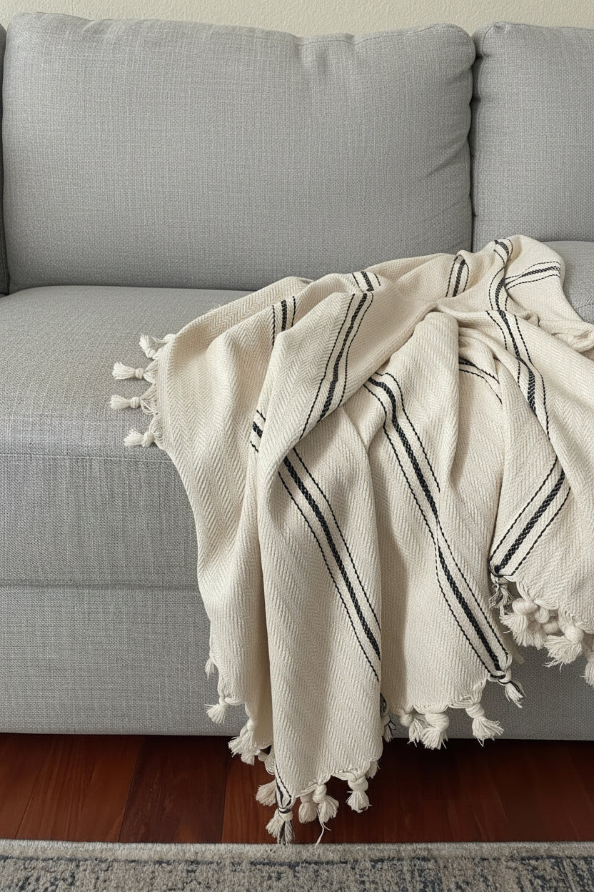 Gray sofa with patterned cushions and a white blanket with black stripes.