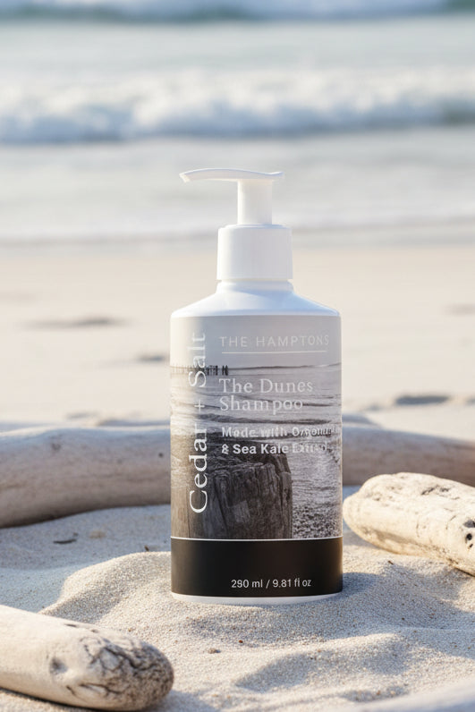 A bottle of The Hemp & Co. Cedar Sit shampoo with a white pump dispenser and a gray-and-black label, set against a dark, rustic background of driftwood and pine branches.