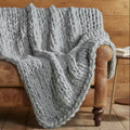Gray chunky knit blanket draped over a brown armchair against a gray wall.