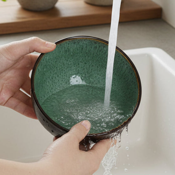 Person washing a green ceramic bowl under running water from a faucet.