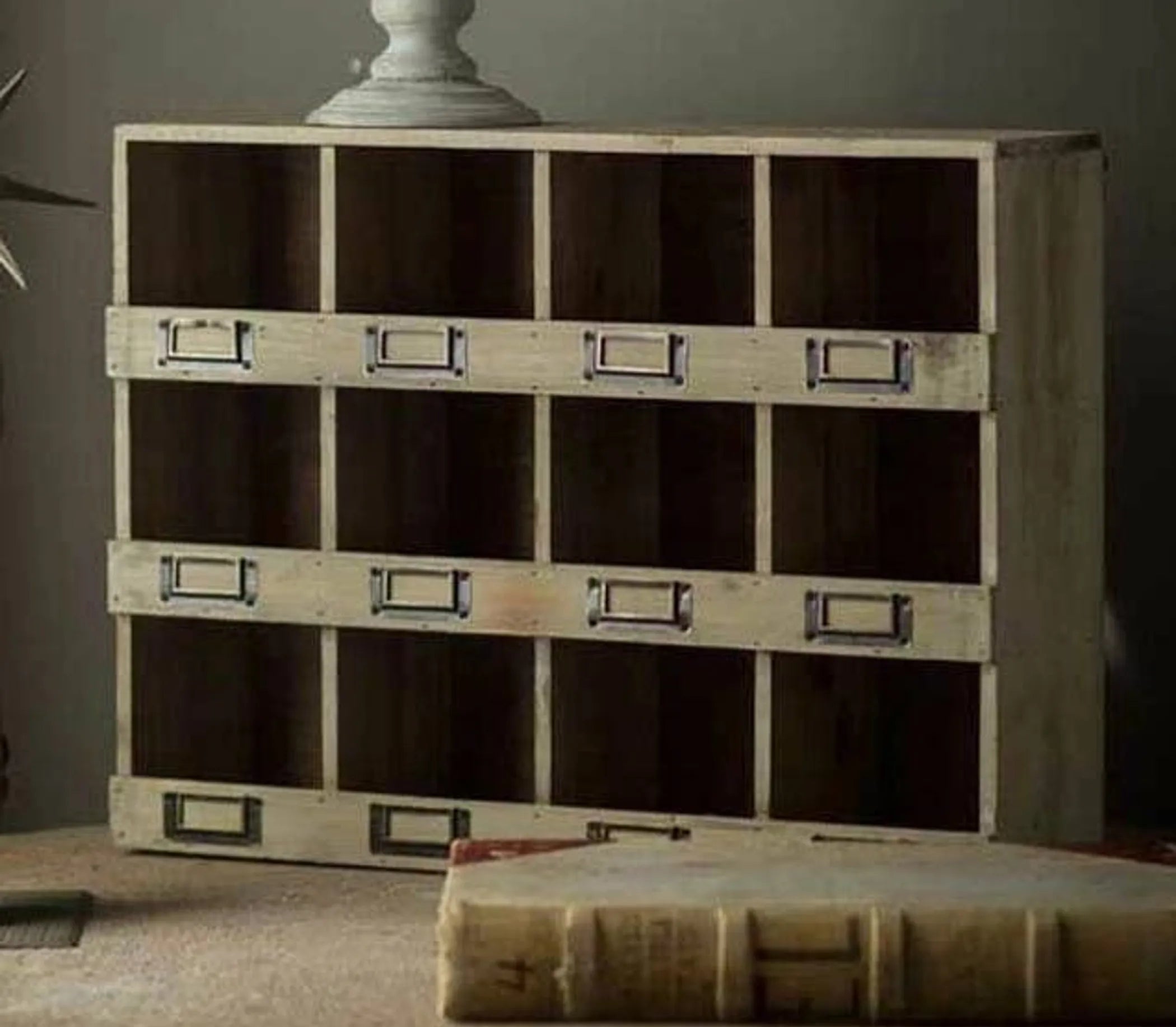 Wooden storage cabinet with metal handles on a table against a gray wall.