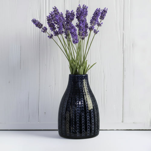 Black textured vase with lavender flowers on a light wooden surface